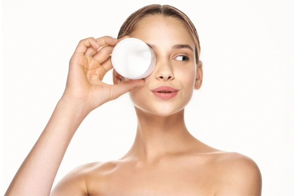 Młoda dziewczyna o jasnych włosach przykłada do twarzy słoiczek z kremem peptydowym